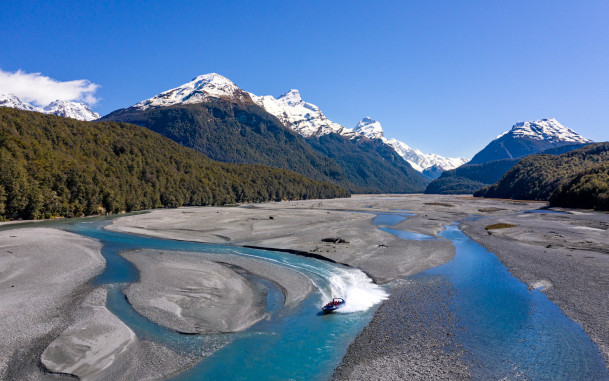Jet boat speeding along the Dart River with snow-capped mountains in Mount Aspiring National Park