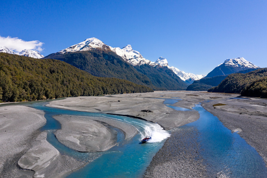 Jet boat speeding along the Dart River with snow-capped mountains in Mount Aspiring National Park