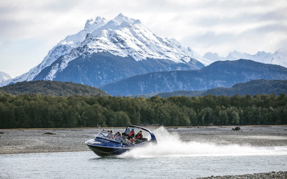 Wilderness Jet boat speeding along the Dart River, with snow-capped mountains in the background