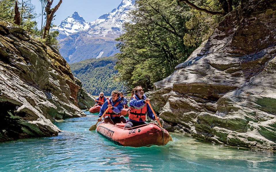 Couple exploring Dart River in Funyak inflatable canoes with snow-capped peaks and forest backdrop