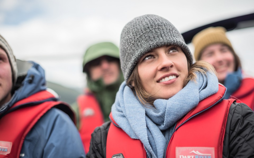 Close-up of a visitor on a jet boat, wearing a life jacket and beanie, gazing at the surrounding scenery