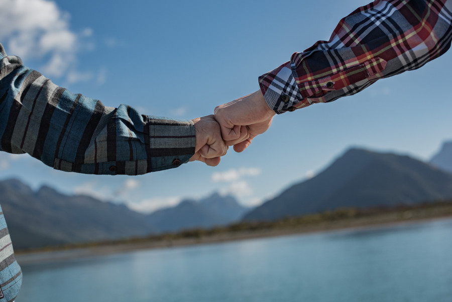 Two hands touching knuckles with Dart River and mountains in the background