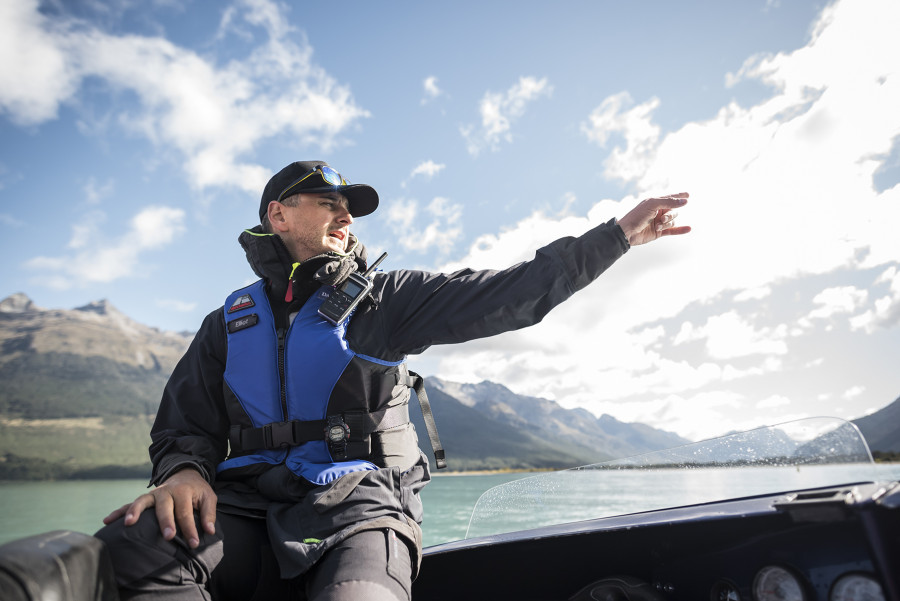 Guide seated on a jet boat, pointing out the surrounding scenery with mountains in the background