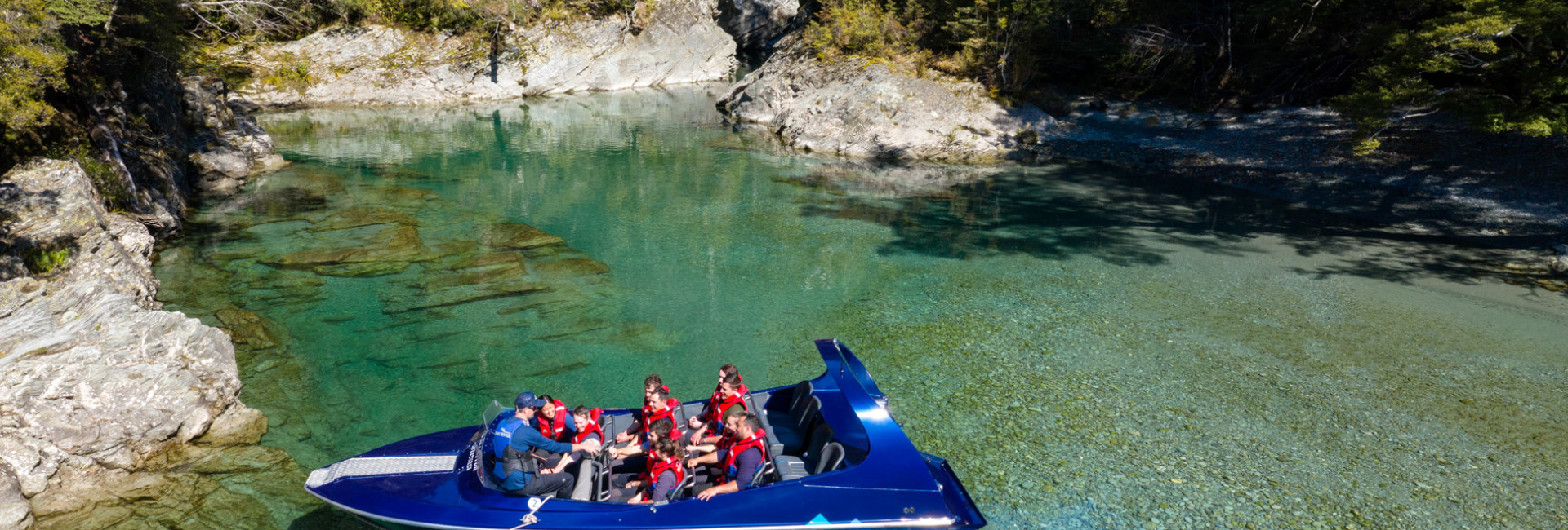 Guide talking to passengers on a Wilderness Jet boat on the Dart River with trees behind