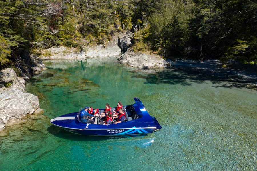 Guide talking to passengers on a Wilderness Jet boat on the Dart River with trees behind